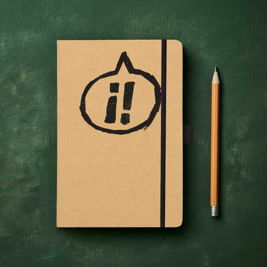 Exclaim Yerself Recycled Kraft paper hardcover notebook, containing 100 pages of lined recycled paper, with recycled closure loop and pen loop, pictured against a dark green textured background next to a pencil. The cover is printed with our logo of two exclamation marks ¡! inside a speech bubble pointing to the top of the notebook.