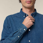 Man adjusting the collar of a mid wash blue denim shirt against a neutral background