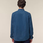 Back view of a man wearing the mid wash blue men's denim shirt against a neutral background