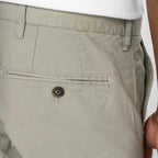 Close-up of a man wearing almond green coloured chino shorts, showing the back pocket with a recycled button closure on the rear pocket, and belt loops, against a neutral background.