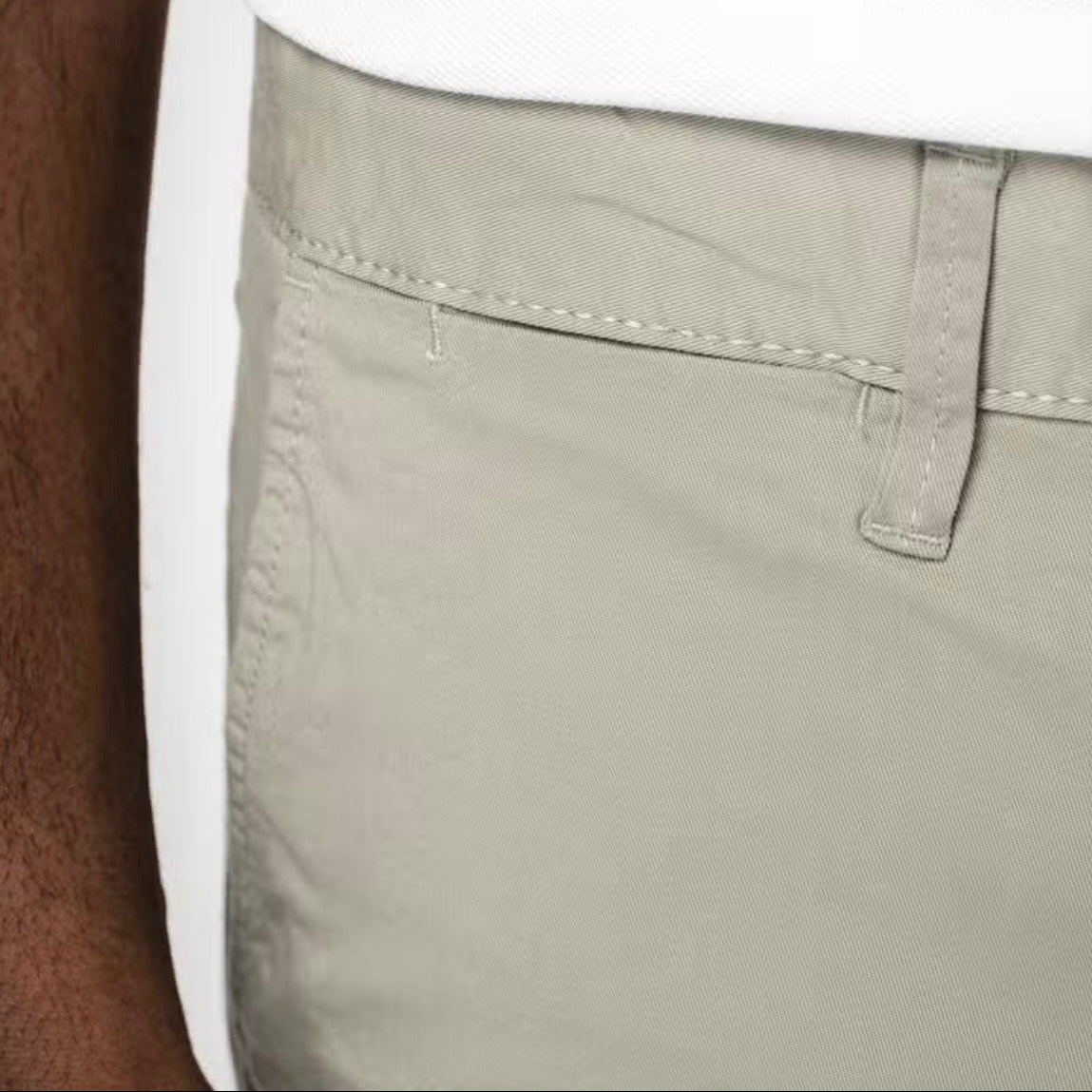 Close-up of a man wearing almond green coloured chino shorts, with belt loops, side pocket, and ticket pocket visible, against a neutral background.