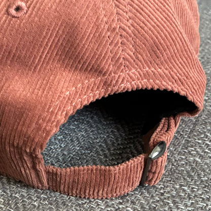Close up detail of the metal slider adjustable fastener at the back of the Redwood organic cotton corduroy cap, featured against a textured grey surface.