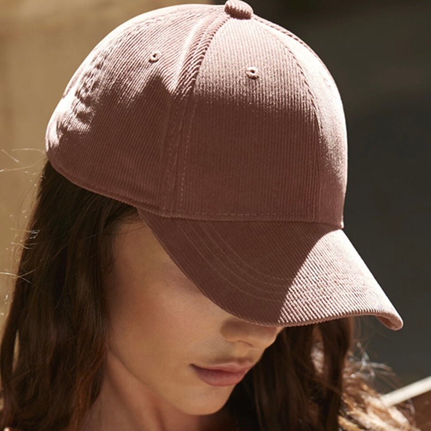 Female model looking down, wearing the Redwood organic cotton corduroy cap, against a blurred background.