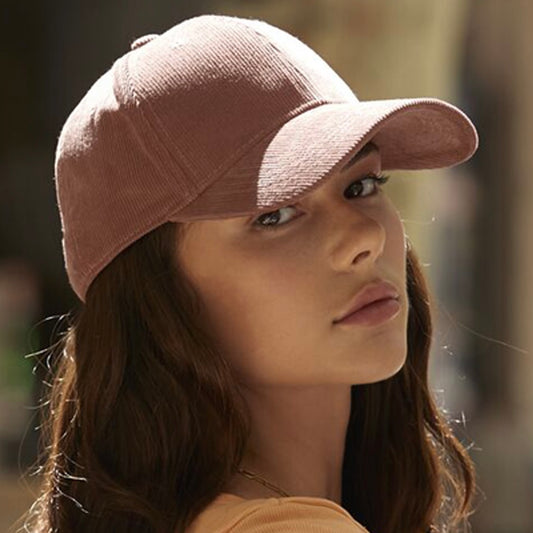 Woman wearing a Redwood corduroy cap, made from 100% organic cotton, against a blurred street view background.